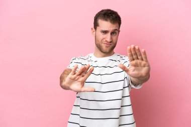 Pembe arka planda izole edilmiş genç beyaz adam sinirden ellerini öne uzatıyor.