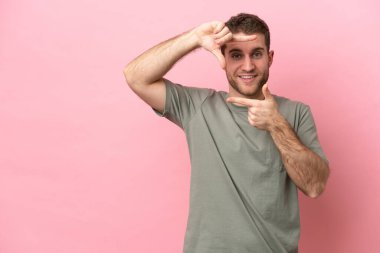 Pembe arka planda izole edilmiş, odaklanan genç beyaz bir adam. Çerçeve sembolü