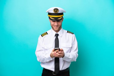 Kafkasyalı uçak pilotu mavi arka planda izole edildi ve cep telefonuyla bir mesaj gönderiyor.
