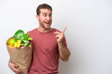 Beyaz arka planda izole edilmiş bir alışveriş poşeti tutan genç beyaz bir adam çözümü fark etmek için parmağını kaldırıyor.
