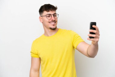 Beyaz arka planda izole edilmiş beyaz tenli yakışıklı bir adam selfie çekiyor.