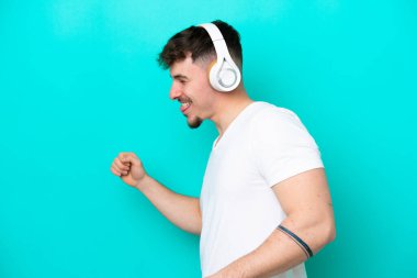 Beyaz tenli yakışıklı adam mavi arka planda izole edilmiş müzik ve dans dinliyor.