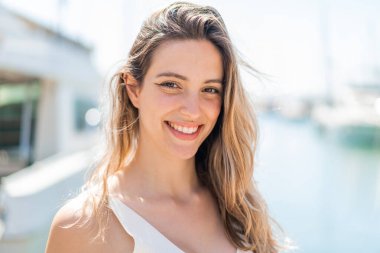 Genç, güzel bir kadın açık havada, mutlu bir ifadeyle.