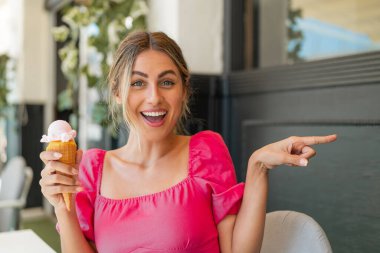 Açık havada kornet dondurması olan genç sarışın kadın şaşırdı ve parmağını yana çevirdi.