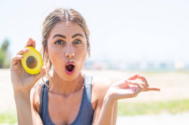 Avokado tutan genç sarışın kadın şaşırmış ve işaret ediyor.