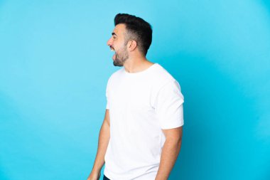 İzole edilmiş mavi arka planda beyaz bir adam yan yana gülüyor.