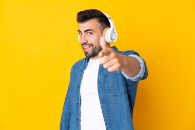 İzole edilmiş sarı arka plan üzerinde beyaz bir adam müzik dinliyor ve ön tarafı işaret ediyor.