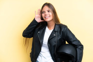 Sarı arka planda izole edilmiş motosiklet kasklı beyaz bir kadın elini kulağına koyarak bir şeyler dinliyor.