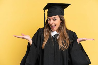 Genç üniversite mezunu, sarı arka planda şok olmuş bir yüz ifadesiyle izole edilmiş.