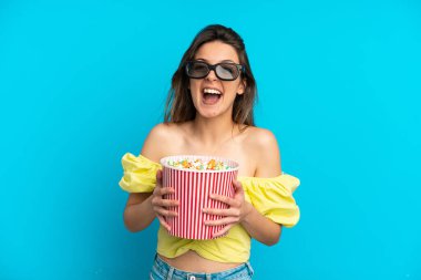 Mavi arka planda 3 boyutlu gözlüklü ve elinde koca bir kova patlamış mısır tutan beyaz bir kadın.