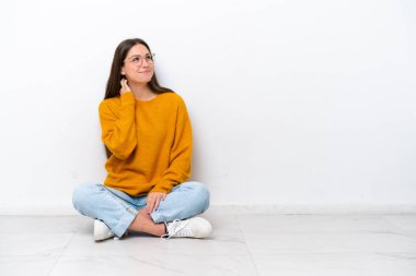 Genç bir kız beyaz arka planda izole bir şekilde yerde oturuyor.