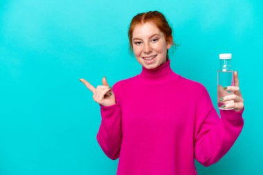 Mavi arka planda izole edilmiş bir şişe suyu olan beyaz, genç bir kadın şaşırmış ve parmağıyla kenarı işaret ediyor.