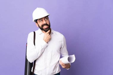 Miğferli genç bir mimar. Mor arka planının planlarını tutuyor. Şüpheleri var.