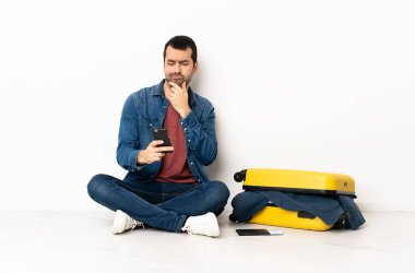 Beyaz tenli yakışıklı bir adam bavul dolusu kıyafetle yerde oturmuş düşünüyor ve bir mesaj yolluyor.