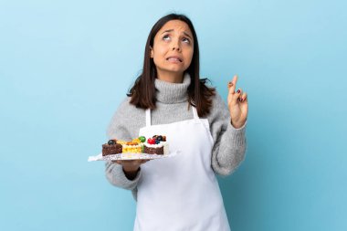 Pasta şefi, izole edilmiş mavi arka planda büyük bir pasta tutuyor ve en iyisini diliyor..