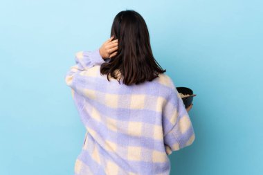 Genç esmer, melez bir kadın elinde bir kase erişteyle arka planda izole edilmiş mavi arka planda durup şöyle düşünüyor:.