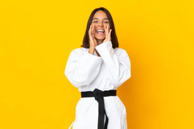 Sarı arka planda karate yapan genç bir kadın bağırıyor ve bir şeyler söylüyor.