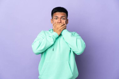 Genç Ekvadorlu adam, mor arka planda izole edilmiş, ağzı elleriyle kapatıyor.
