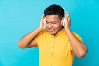 Genç Ekvadorlu adam mavi arka planda izole edilmiş müzik dinliyor.