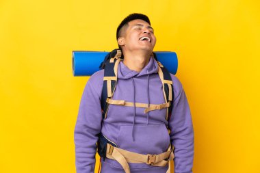 Sarı arka planda büyük bir sırt çantası olan genç dağcı gülüyor.