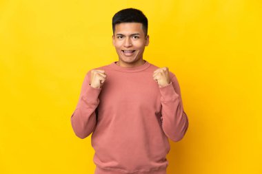 Sarı arka planda izole edilmiş genç Ekvadorlu zaferi kutluyor.