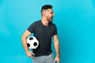 Futbolcu mavi arka planda izole edildi. Yan pozisyonda gülüyor.