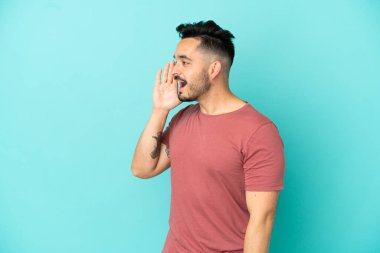 Mavi arka planda izole edilmiş genç beyaz adam ağzı sonuna kadar açık bağırıyor.