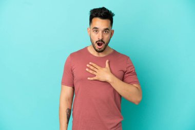 Mavi arka planda izole edilmiş genç beyaz adam sağa bakarken şaşırdı ve şok oldu.