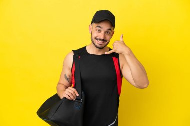 Spor çantalı beyaz bir genç, sarı arka planda izole edilmiş telefon jesti yapıyor. Bana geri dönüş işareti ver.