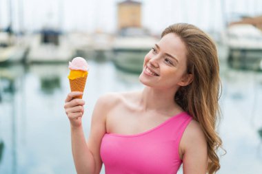 Kornet dondurmalı genç kızıl kadın gülümserken yukarı bakıyor.