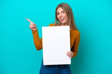 Kafkasyalı genç bir kadın mavi arka planda izole edilmiş, elinde boş bir levha ve işaret eden bir tarafı var.