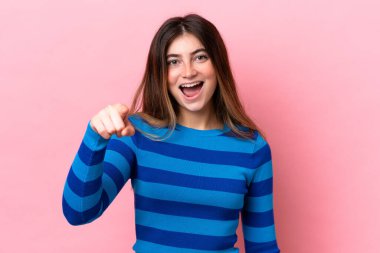 Pembe arka planda izole edilmiş genç beyaz kadın şaşırmış ve ön tarafı işaret ediyor.