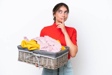 Beyaz arka planda izole edilmiş çamaşır sepetini tutan genç beyaz bir kadın yukarı bakarken şüpheleri var.