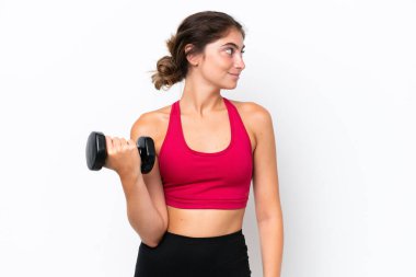 Beyaz arka planda halter kaldıran beyaz tenli genç bir kadın yan tarafa bakıyor.