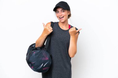 Spor çantalı genç bir kadın beyaz arka planda izole edilmiş. Baş parmakları havada ve gülümsüyor.