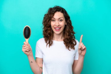 Mavi arka planda saç fırçası tutan beyaz bir kadın harika bir fikre işaret ediyor.