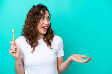 Mavi arka planda diş fırçalayan beyaz bir kadın. Şaşırtıcı bir yüz ifadesi var.