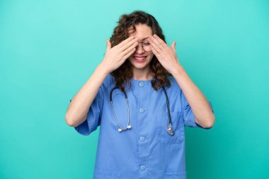 Genç beyaz kadın, mavi arka planda izole edilmiş, gözleri elle kapatılmış.