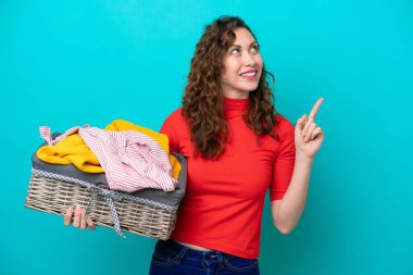 Mavi arka planda izole edilmiş çamaşır sepeti tutan beyaz bir kadın harika bir fikre işaret ediyor.