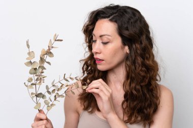 Beyaz arka planda, elinde okaliptüs dalı tutan beyaz tenli bir kadın. Portreyi kapat