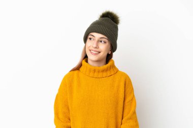 Kışlık şapkalı genç kız beyaz arka planda izole edilmiş bir şekilde yukarı bakarken bir fikir düşünüyor.