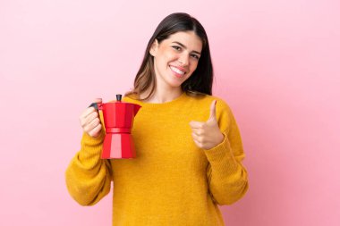 Pembe arka planda izole edilmiş kahve makinesini tutan genç bir İtalyan kadın baş parmak işareti yapıyor.