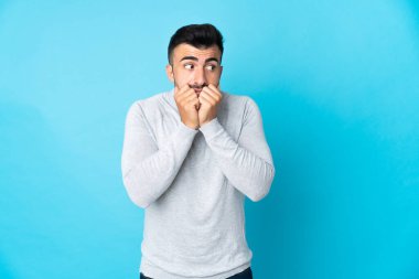 İzole edilmiş mavi arka planda beyaz bir adam gergin ve korkmuş bir şekilde elleriyle suni teneffüs yapıyor.