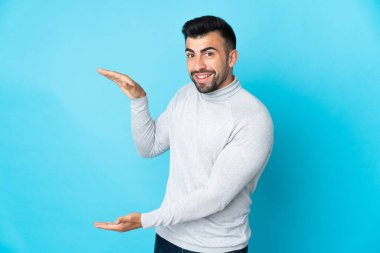 İzole edilmiş mavi arkaplan üzerinde beyaz bir adam bir reklam eklemek için kopyalama alanı tutuyor