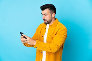 İzole edilmiş mavi arkaplan üzerinde beyaz adam cep telefonuyla bir mesaj ya da e-posta gönderiyor