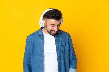 İzole edilmiş sarı arka planda beyaz bir adam müzik dinliyor.