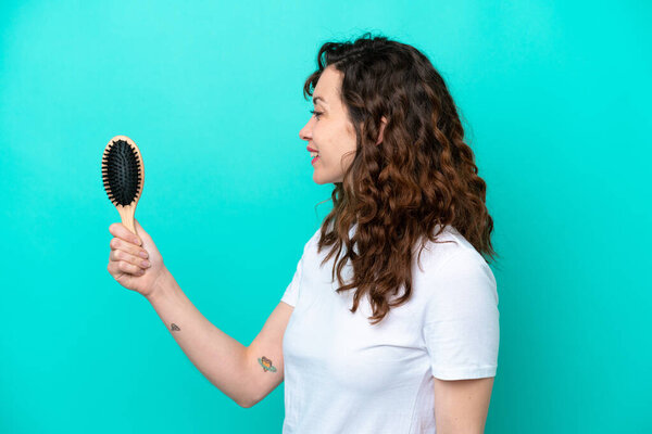 Молодая белая женщина держит расческу на голубом фоне со счастливым выражением лица