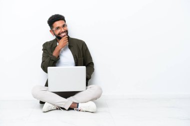 Yerde dizüstü bilgisayarı olan genç Brezilyalı bir adam gözlüklü ve gülümseyen beyaz tenli.