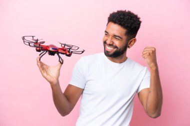 Pembe arka planda insansız hava aracı tutan genç Brezilyalı bir adam zaferi kutluyor.