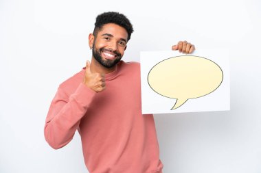 Genç Brezilyalı bir adam beyaz arka planda izole edilmiş. Elinde parmak uçlarında konuşma balonu simgesi olan bir levha var.